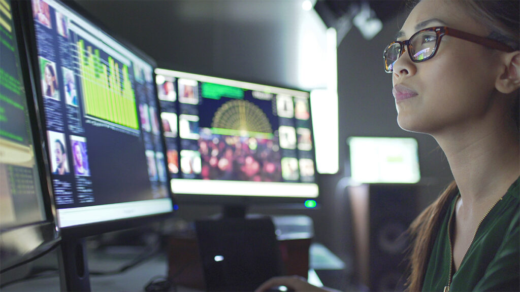 A clinical professional reviewing data on two computer screens.